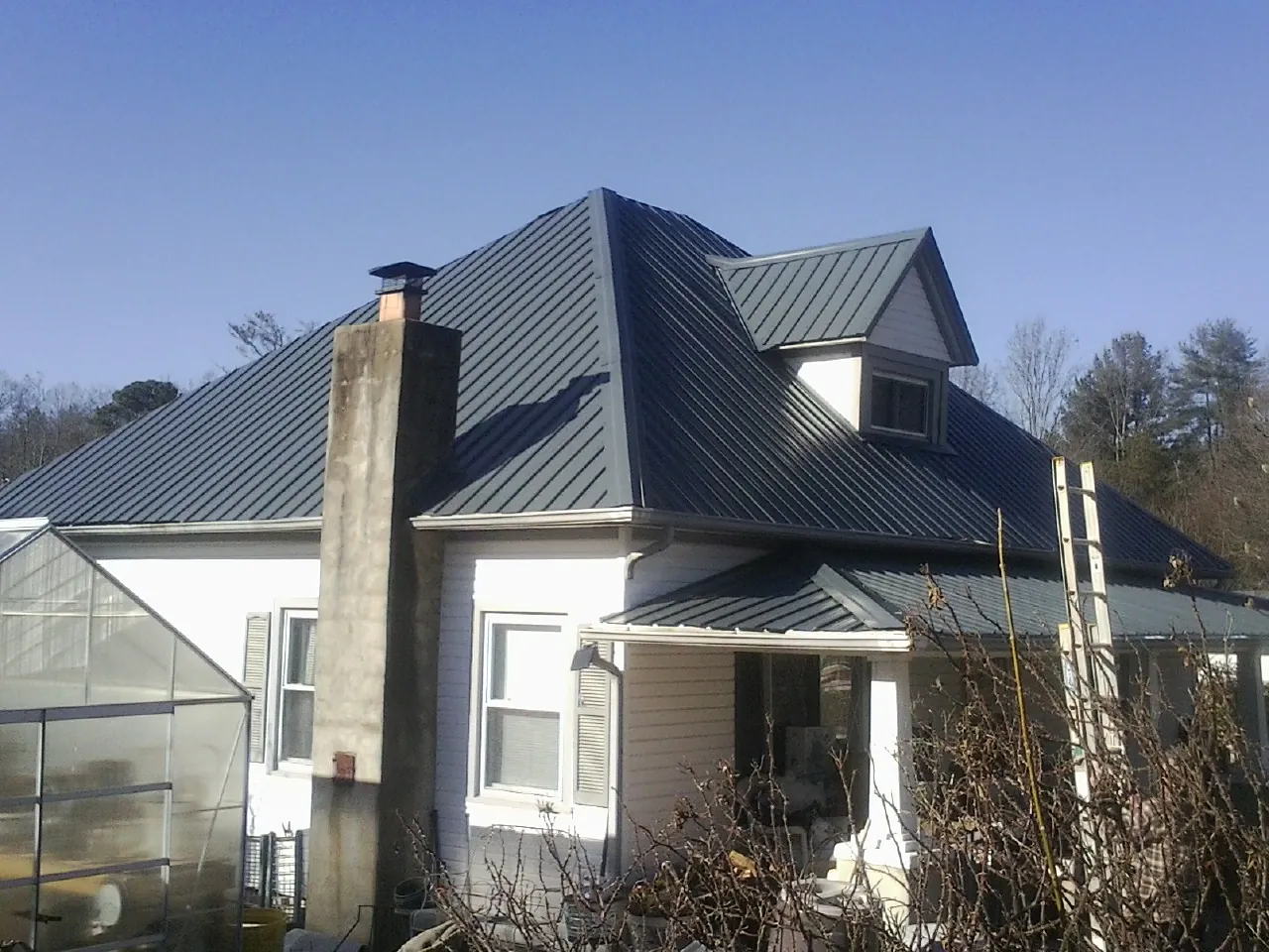 Dark blue standing seam metal roof on a white farmhouse with dormer — Slate & Tile Roof Repair by Roofing Brothers in Cook Springs
