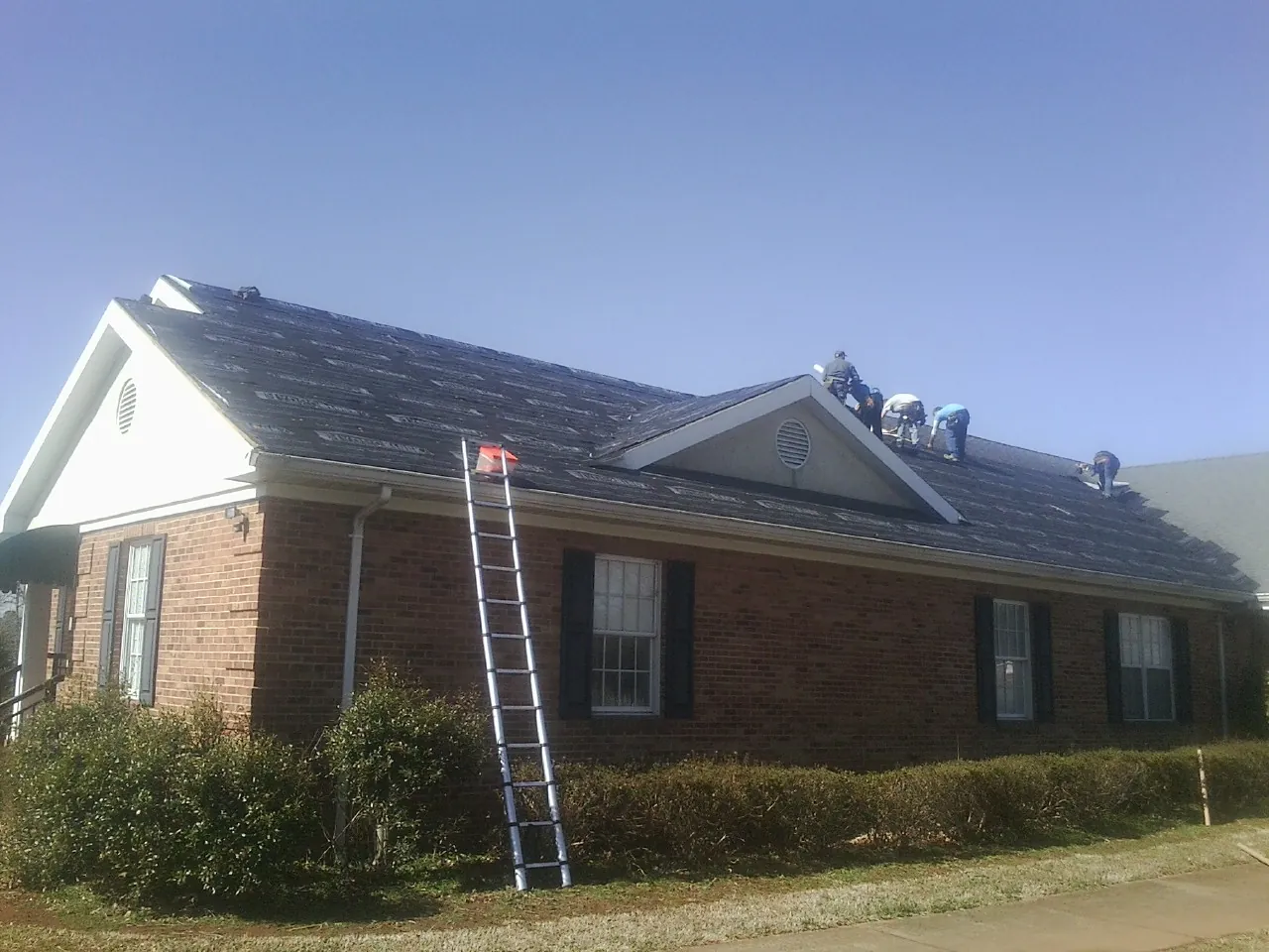 Crew tearing shingles off a brick ranch roof with a ladder set — Emergency Roof Repair work by our crew in Cook Springs