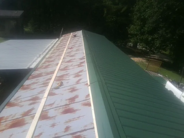 Old rusted panels beside newly installed green metal roofing — Wind Damage Roof Repair by Roofing Brothers in Cook Springs