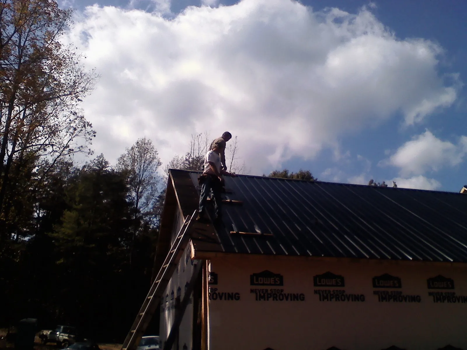Roofer fastening dark metal panels high against a cloudy sky, from a Roof Inspection job in Cook Springs