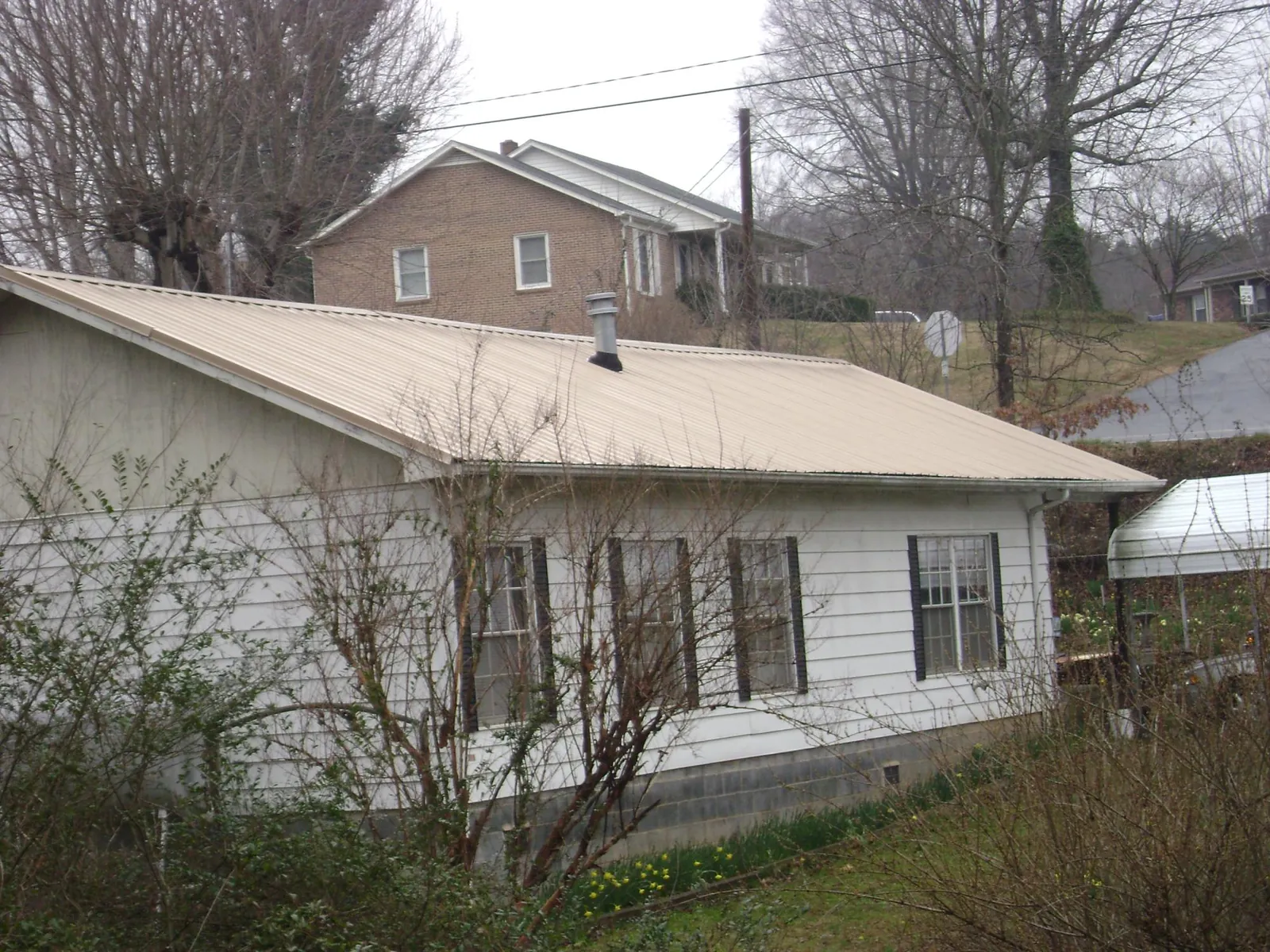 Tan metal roof on a white sided house set into a hillside — Commercial Roofing by Roofing Brothers in Cook Springs